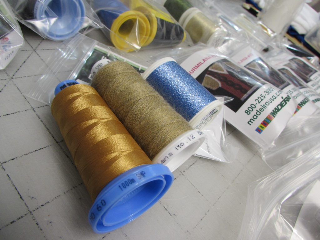 Samples provided by manufacturers provide a low-cost way to test and promote new materials and techniques; here, 60wt thread, thick wool-blend thread, and a metallic-infused twist thread from sample kits are on-deck for testing. 